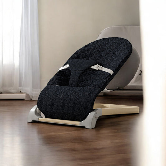 Black baby bouncer chair on a wooden floor with a neutral-colored wall in the background