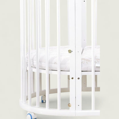 White crib with a white mattress in a minimalistic room.