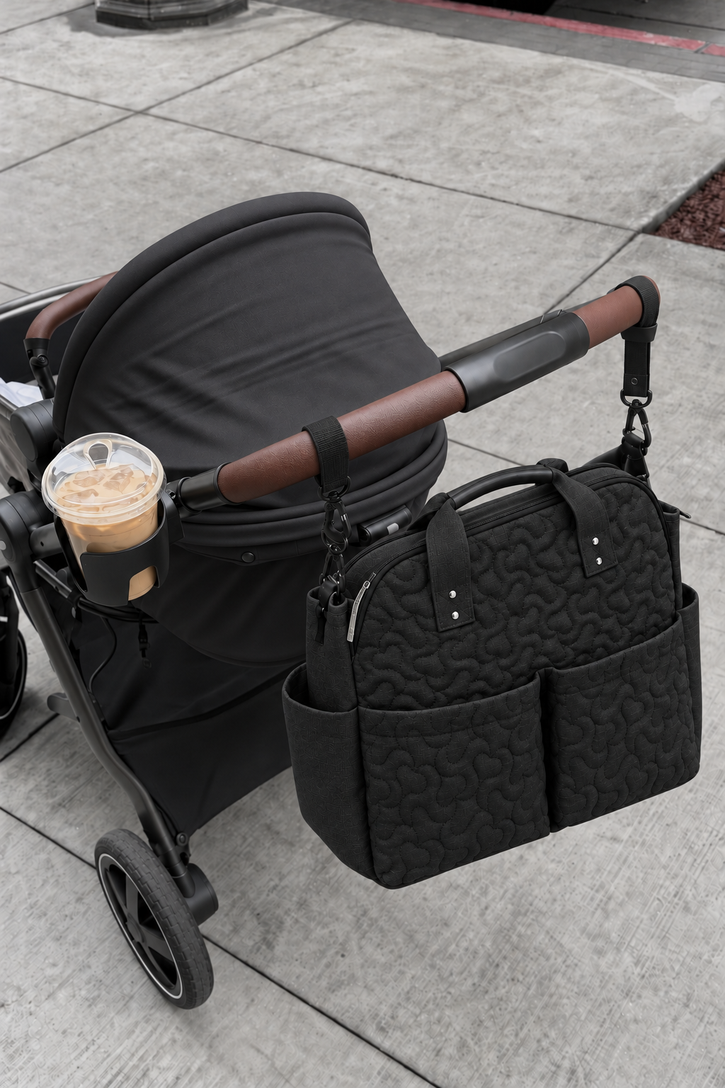 Black quilted changing bag on a black stroller with brown handle and cupholder