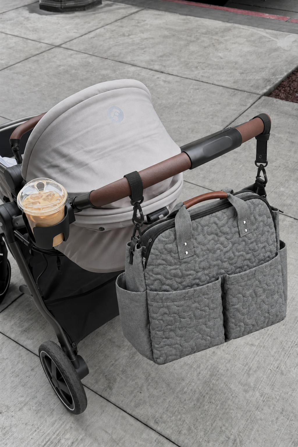 Grey quilted changing bag on a grey stroller with a brown handle and cupholder