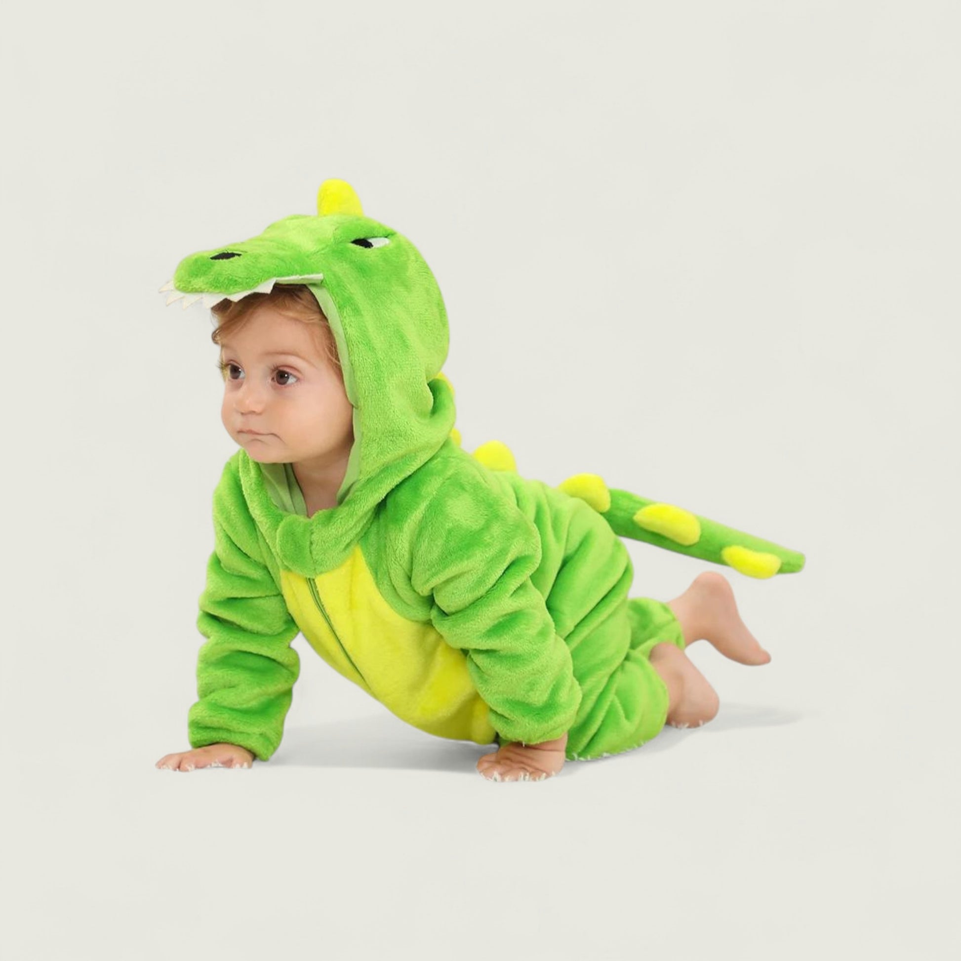 Baby in a green dinosaur costume on a light gray background
