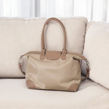 Beige handbag on a beige sofa with a white curtain background