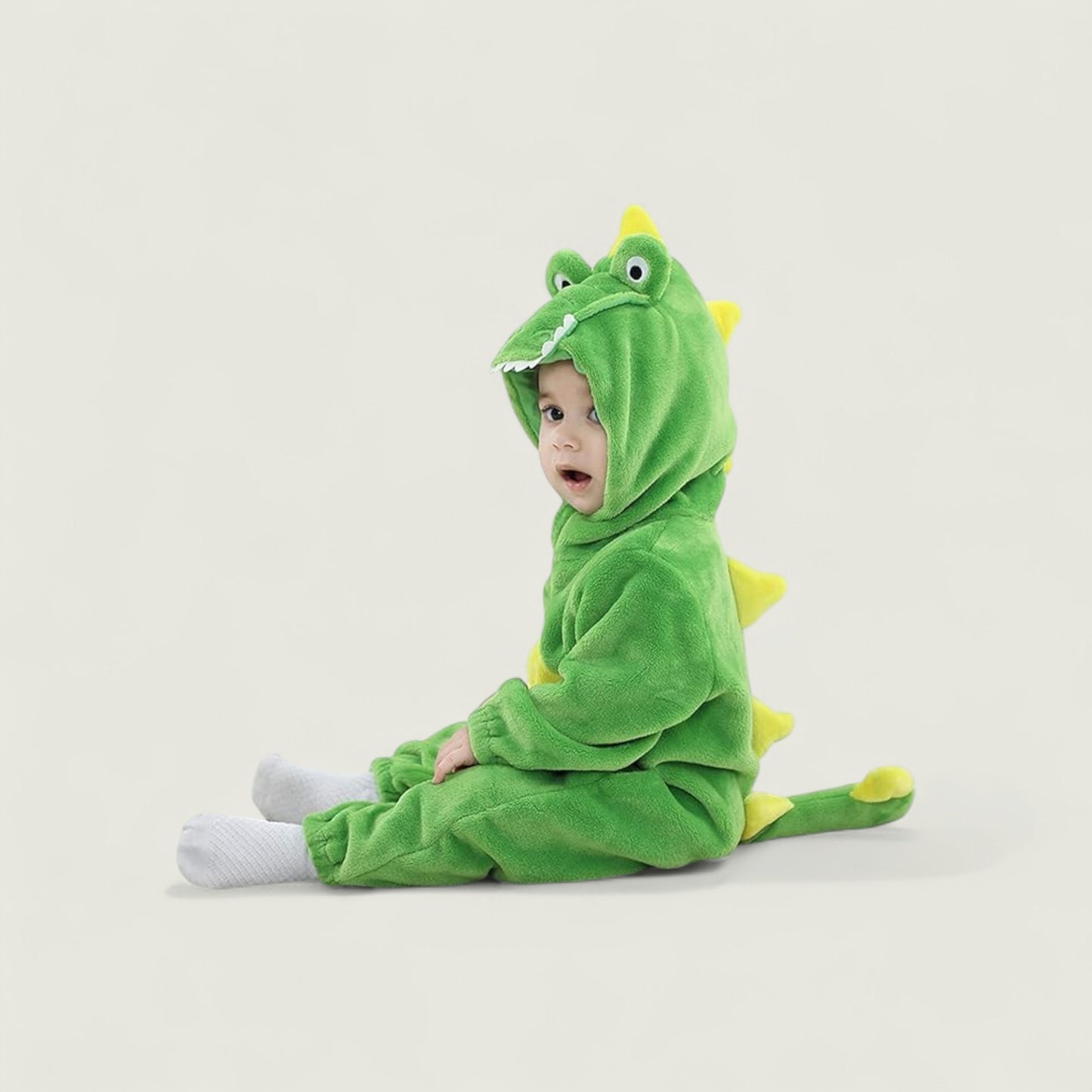 Child wearing a green dinosaur onesie on a light gray background
