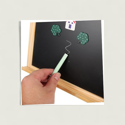 Hand holding a light green chalk near a small blackboard with green leaves and a white flag.