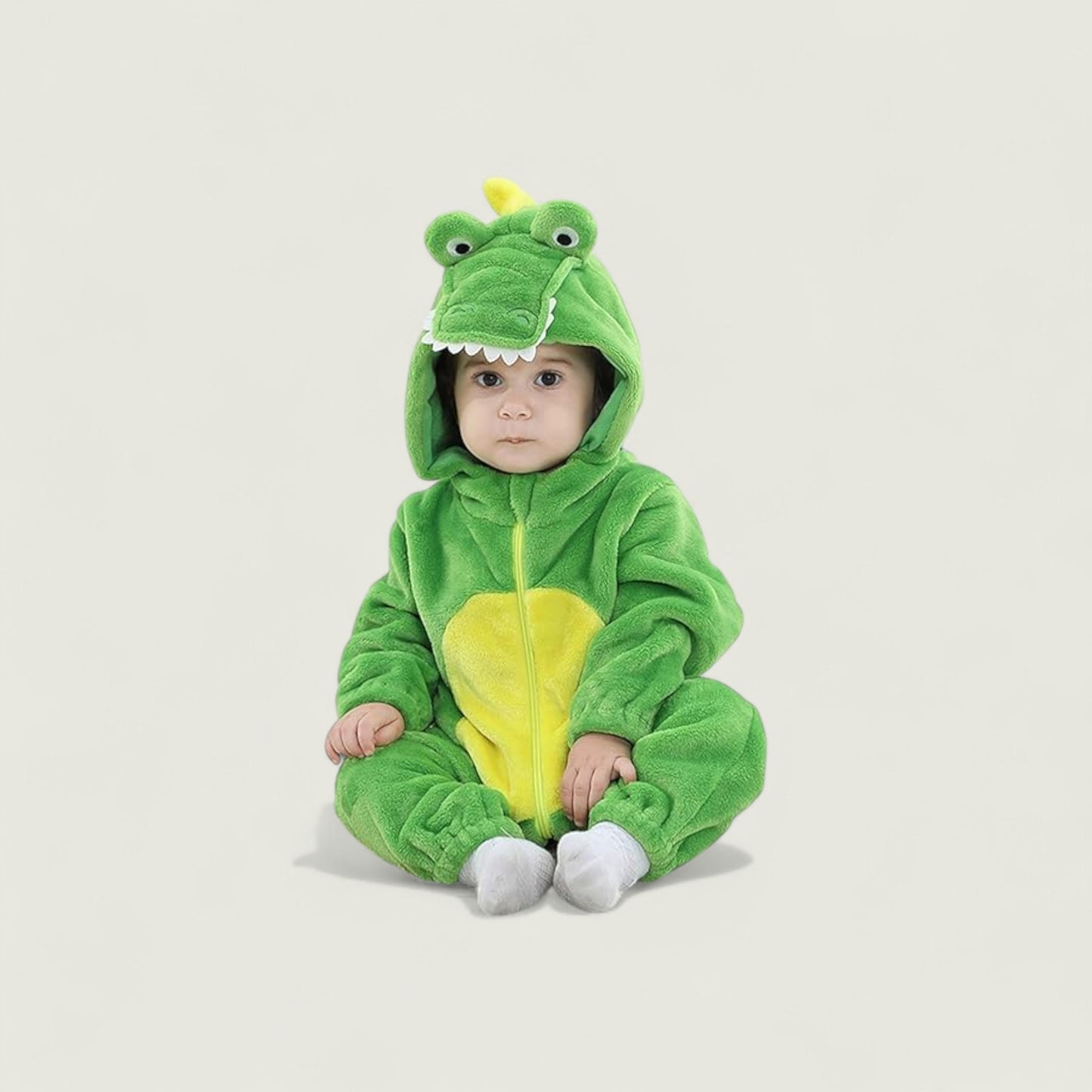 Baby in a green dinosaur onesie on a beige background