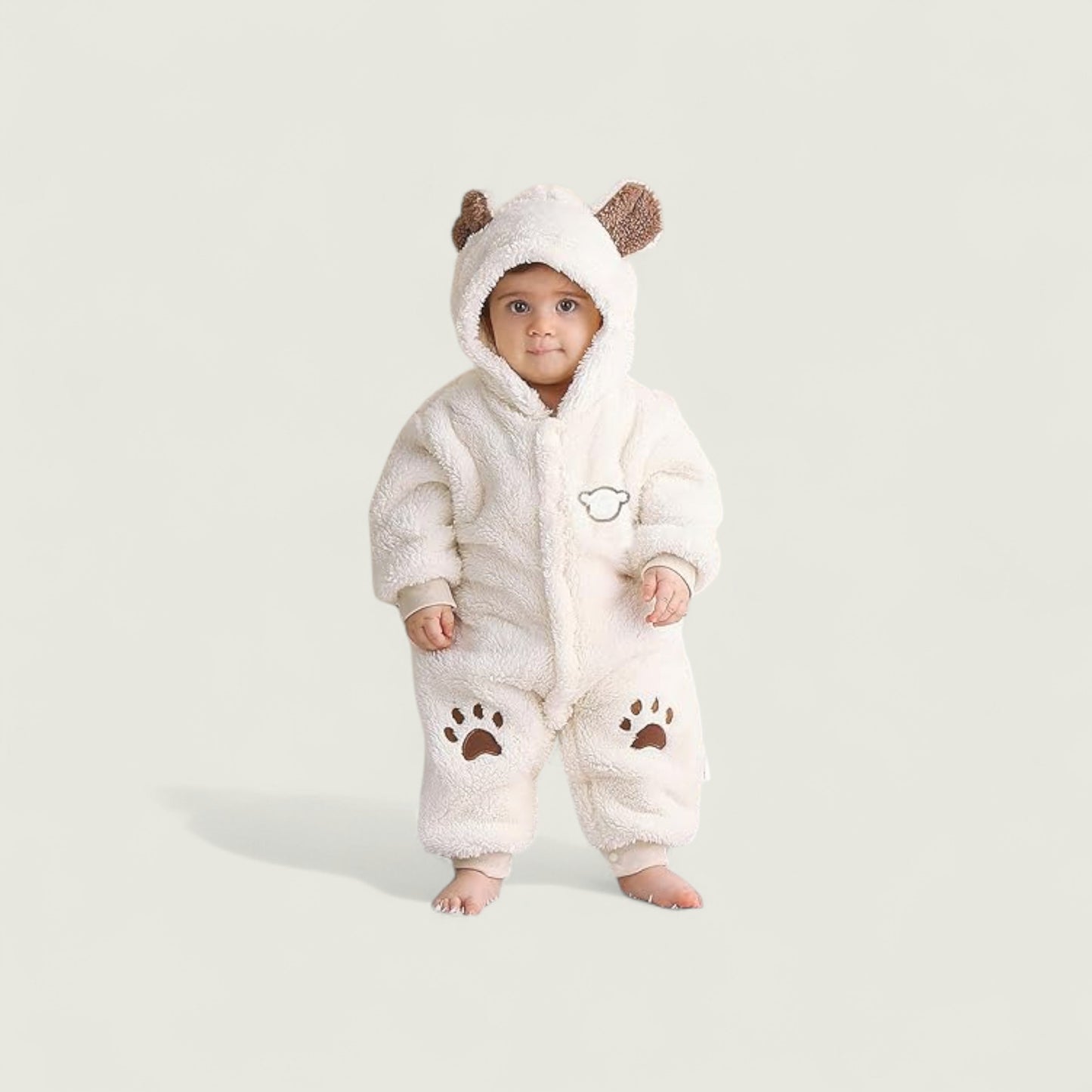 Baby wearing a white fluffy onesie with bear ears and paw prints on a light gray background