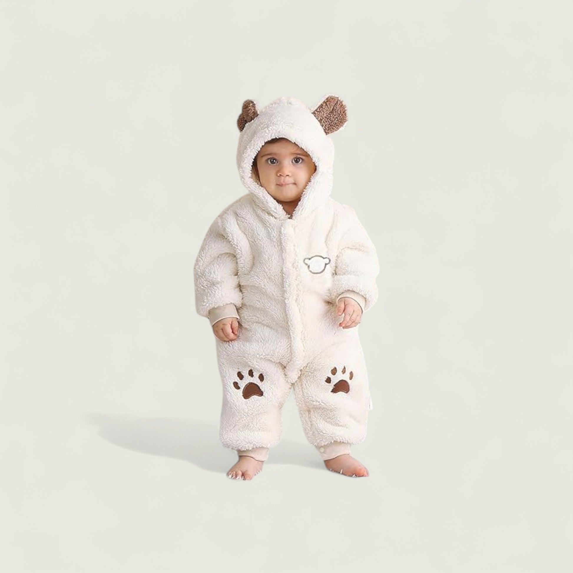 Baby wearing a white fluffy onesie with bear ears and paw prints on a light gray background
