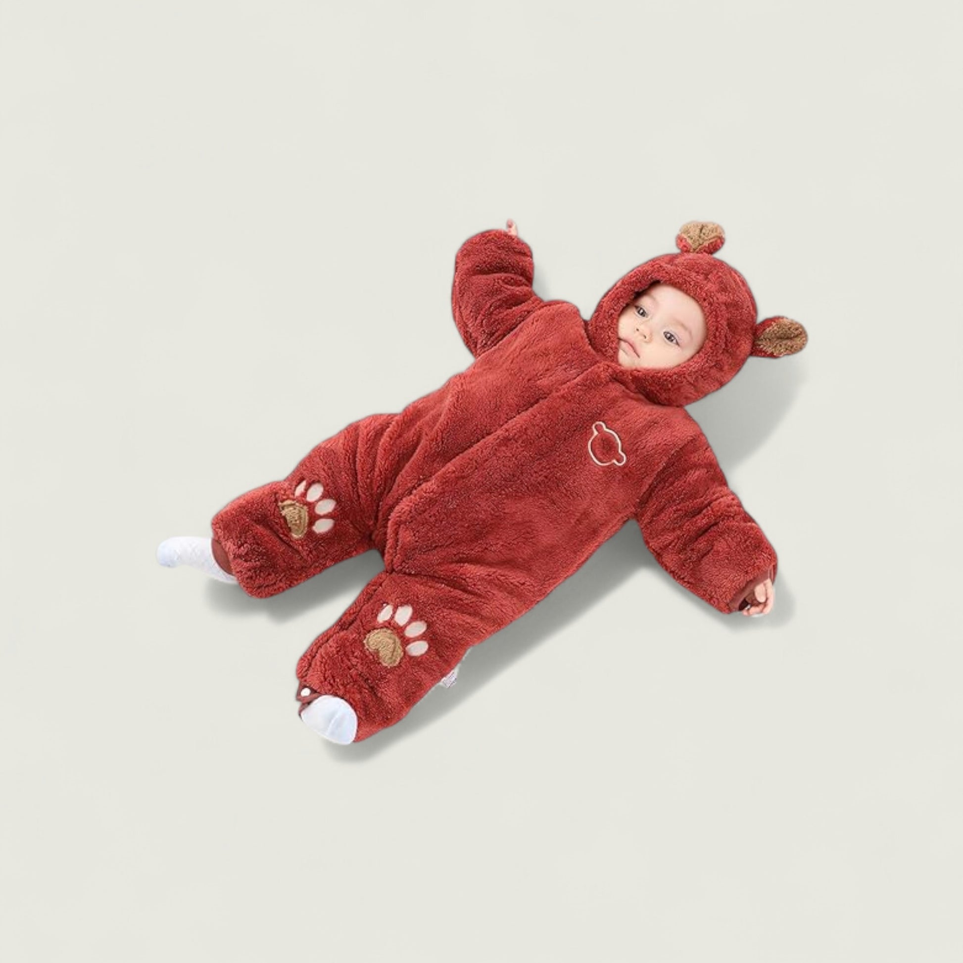 Baby in a red bear-themed onesie lying on a light beige background