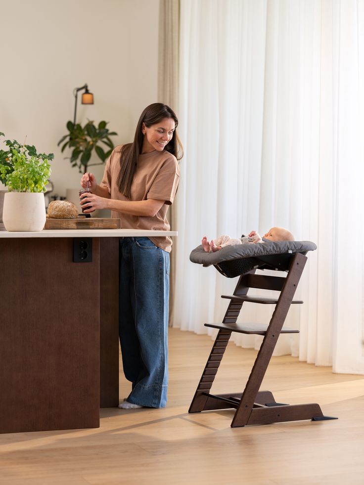 Woman standing at a counter with a baby in a high chair in a home setting