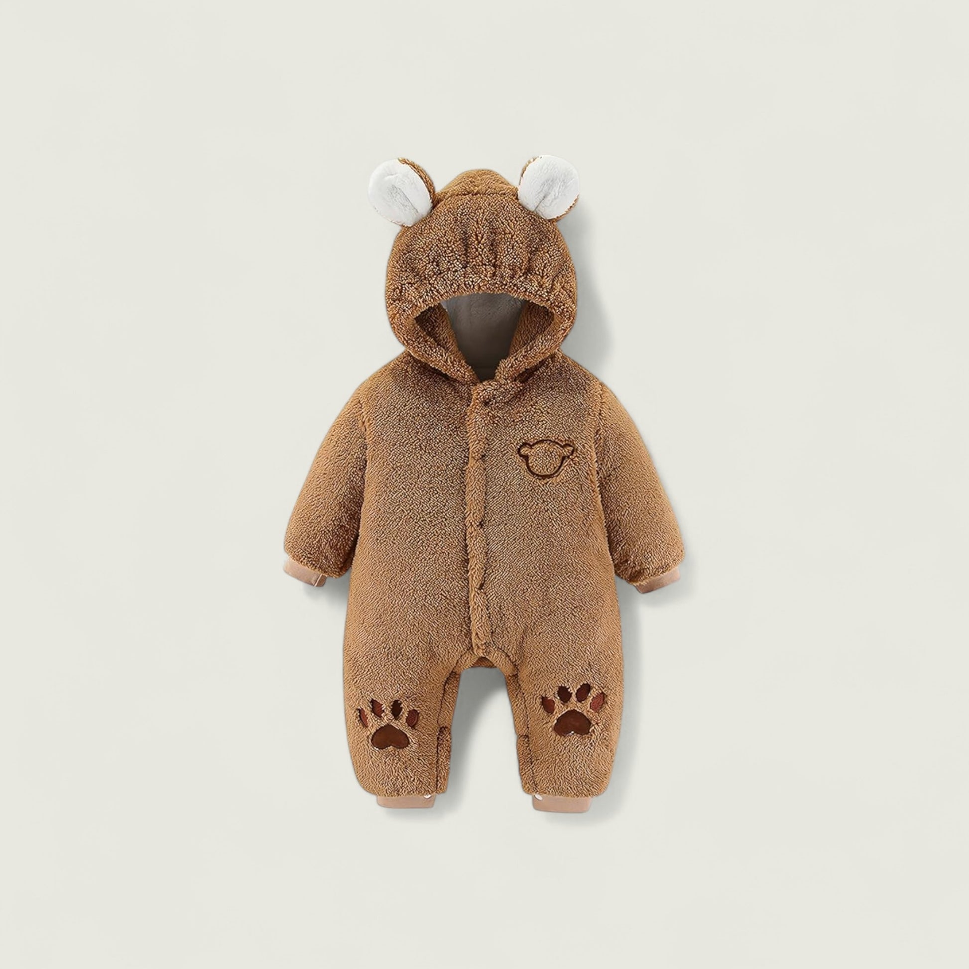 Brown baby onesie with bear ears and paw prints on a beige background