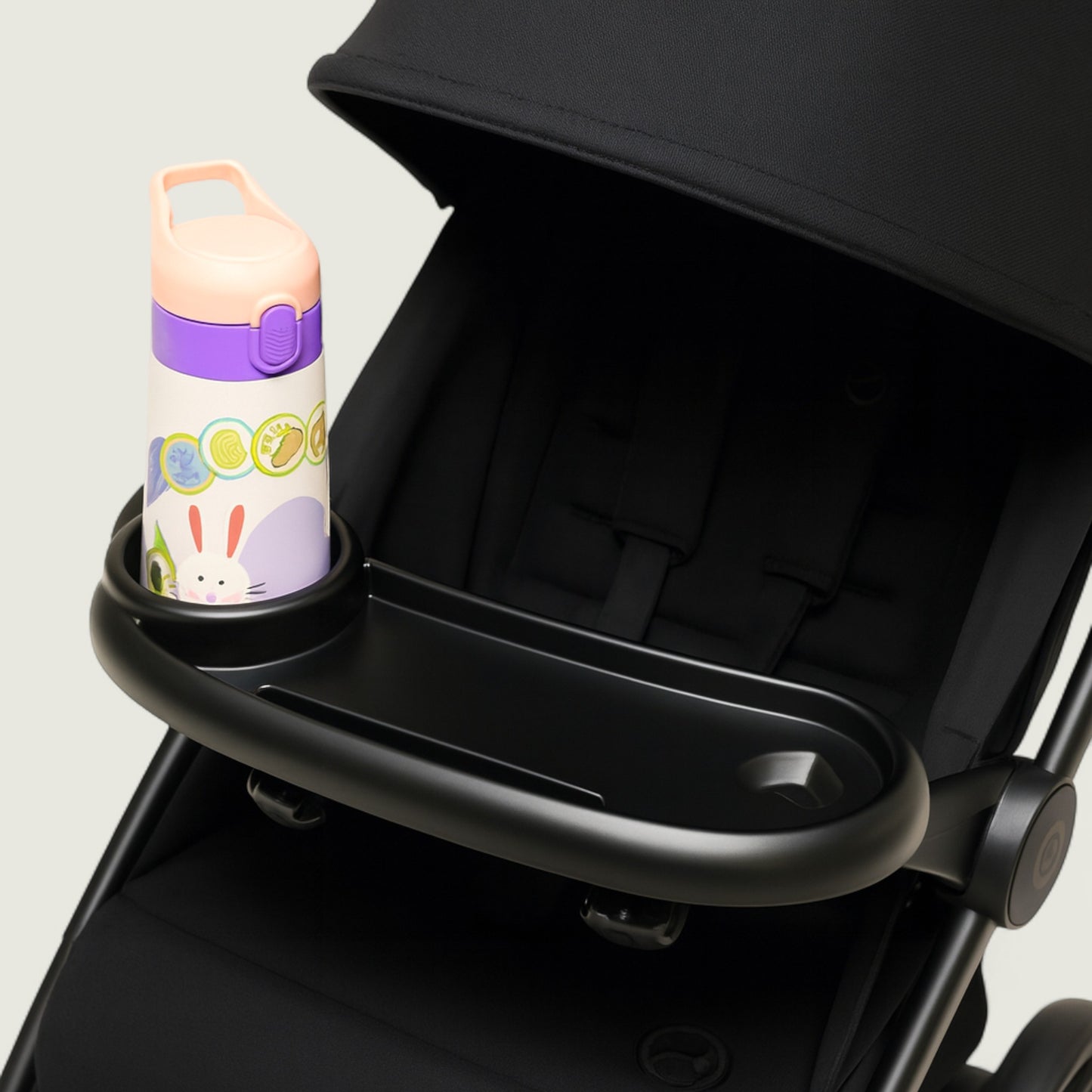 Black stroller with a cup holder containing a colorful water bottle on a light gray background