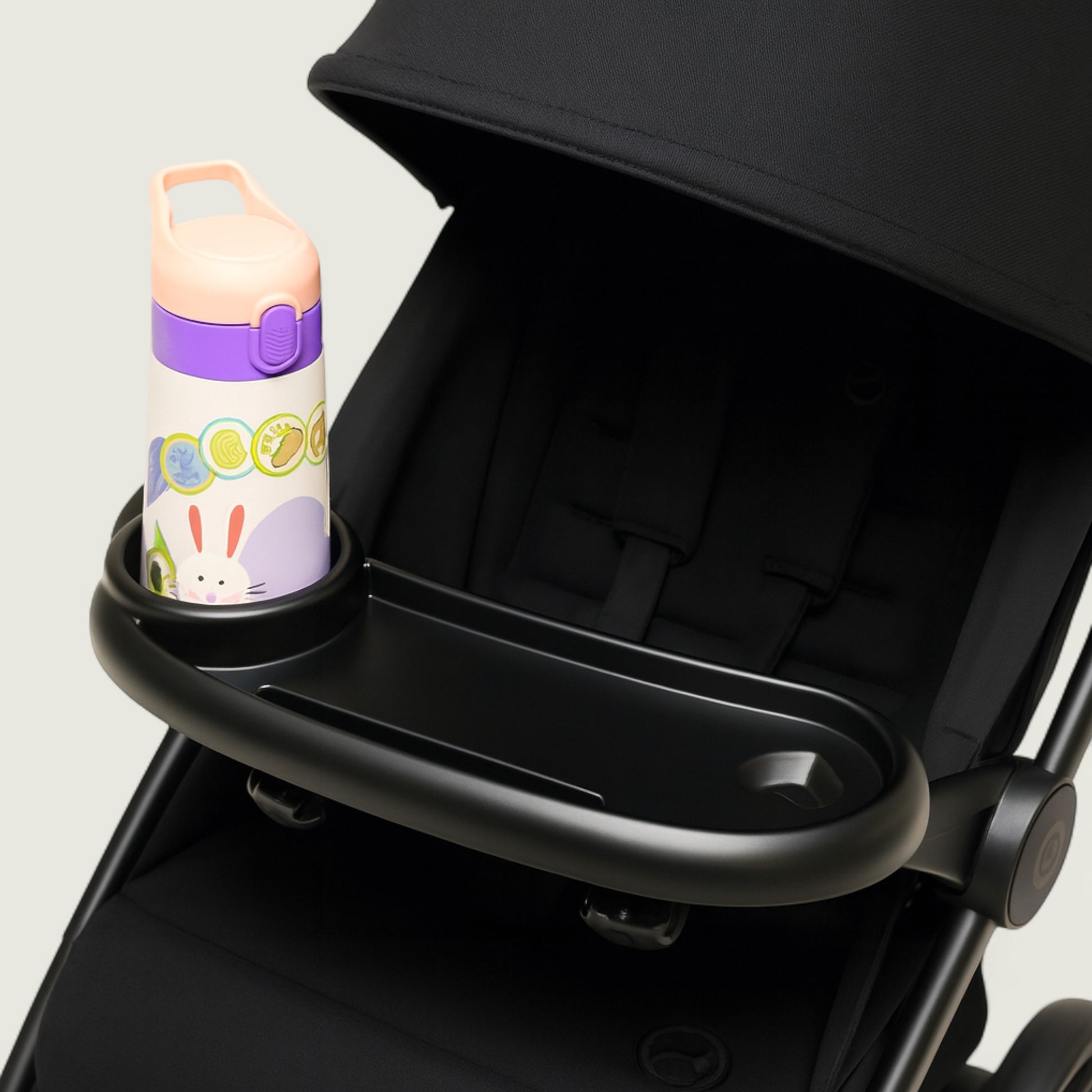 Black stroller with a cup holder containing a colorful water bottle on a light gray background