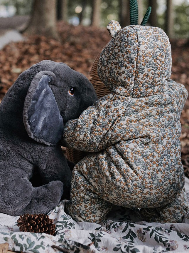 Two plush toys, one gray and one floral-patterned, sitting together on a fabric surface with a natural background.