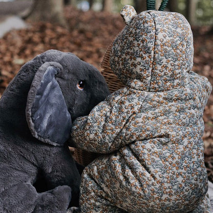 Two plush toys, one gray and one floral-patterned, sitting together on a fabric surface with a natural background.