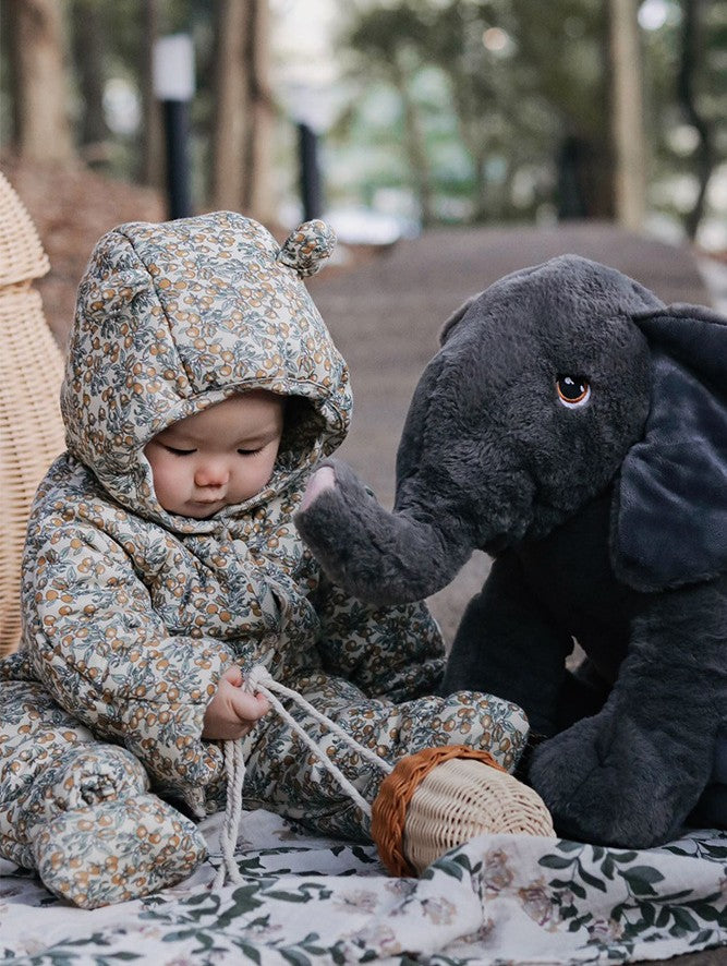 Child in floral hooded outfit playing with a plush toy in an outdoor setting