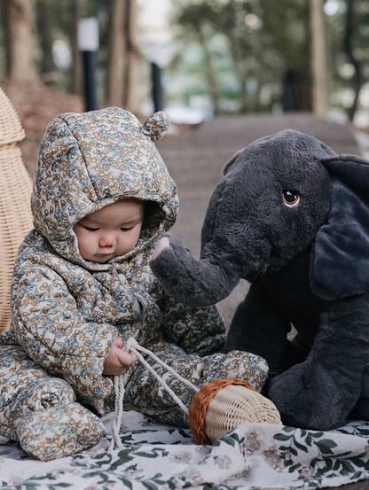 Child in floral hooded outfit playing with a plush toy in an outdoor setting