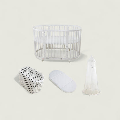 White crib with bassinet, mattress, and canopy on a light beige background