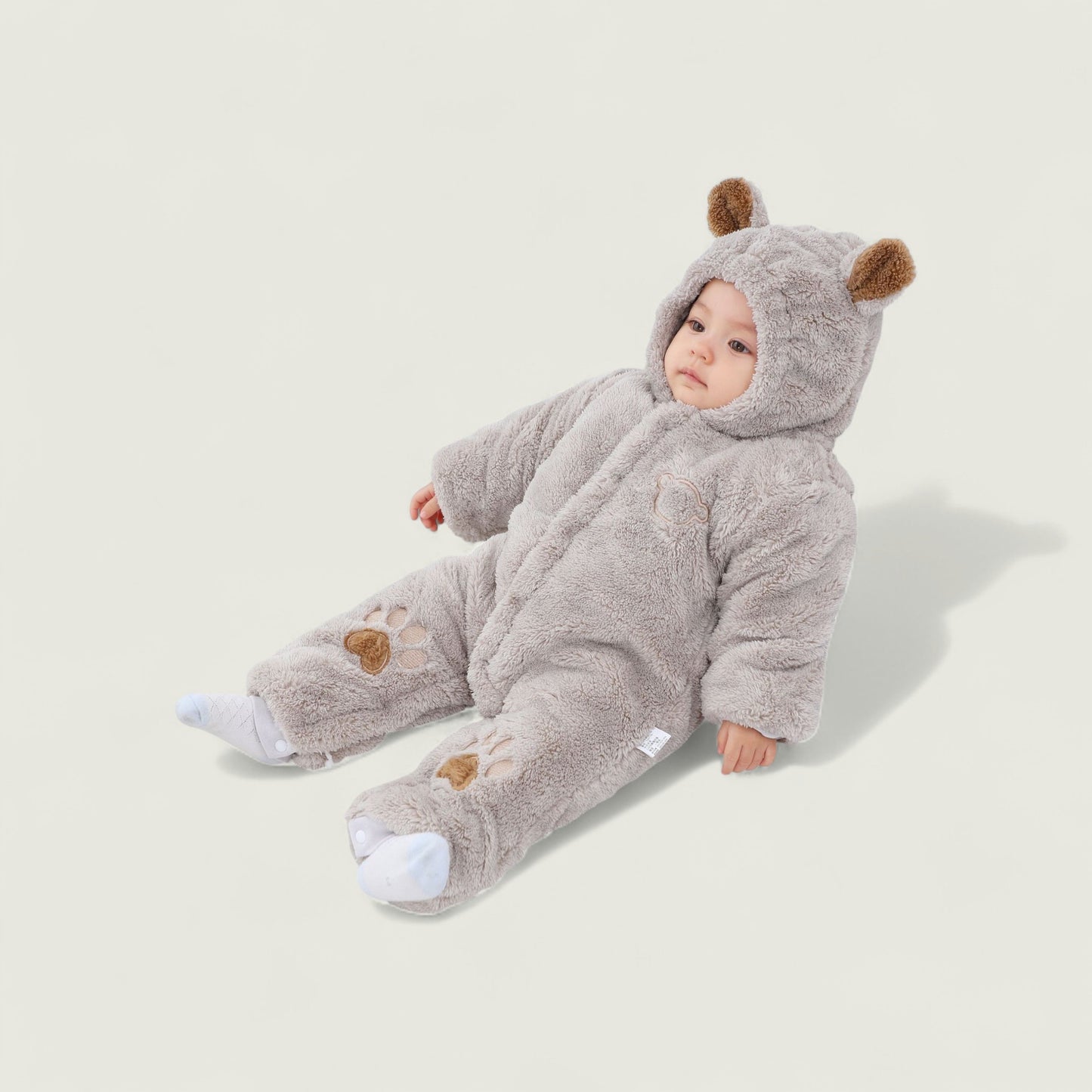 Baby in a gray bear onesie on a light beige background