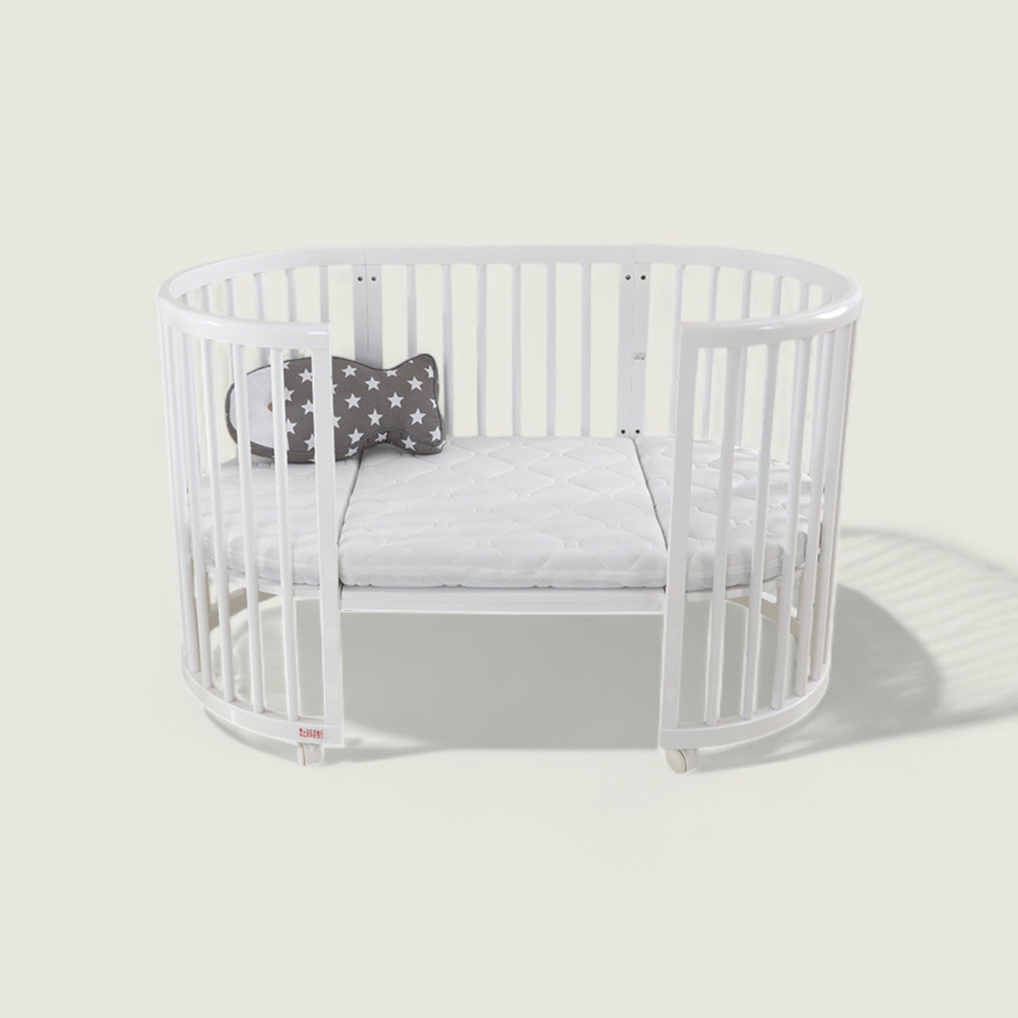White crib with a gray cushion and star-patterned pillow on a light gray background
