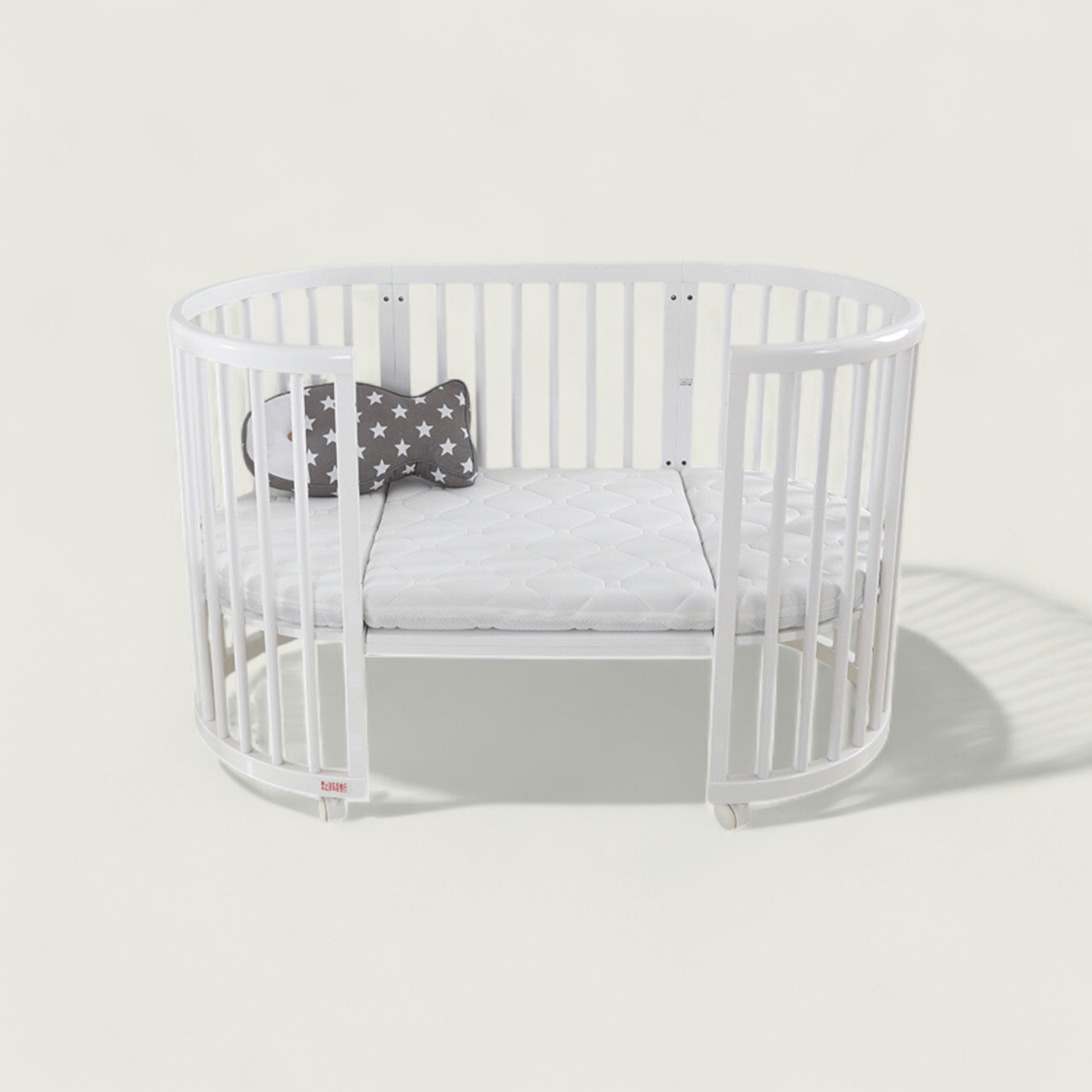 White crib with a gray cushion and star-patterned pillow on a light gray background