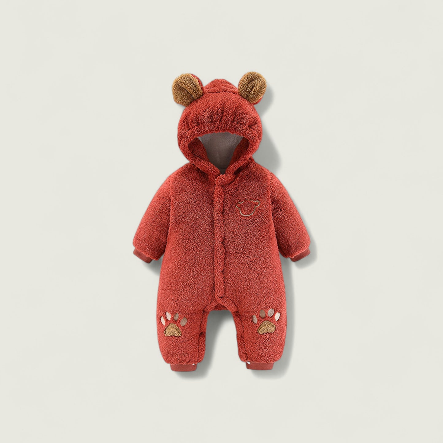 Red baby snowsuit with bear ears and paw prints on a beige background