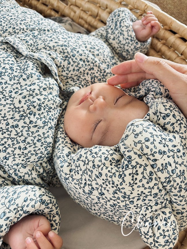 Baby in floral outfit being held by a hand, lying on a textured surface