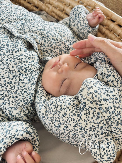 Baby in floral outfit being held by a hand, lying on a textured surface