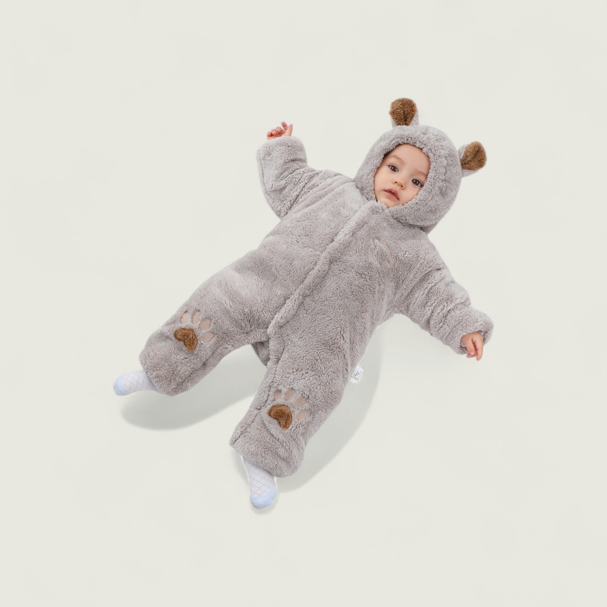Baby in a gray fluffy onesie with bear ears and paw prints on a light background