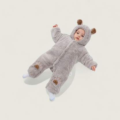 Baby in a gray fluffy onesie with bear ears and paw prints on a light background