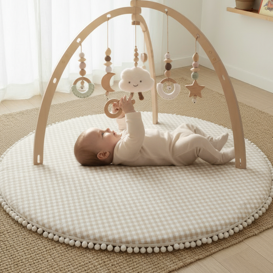 Baby playing with a wooden arch toy on a white mat in a room with curtains and a shelf.
