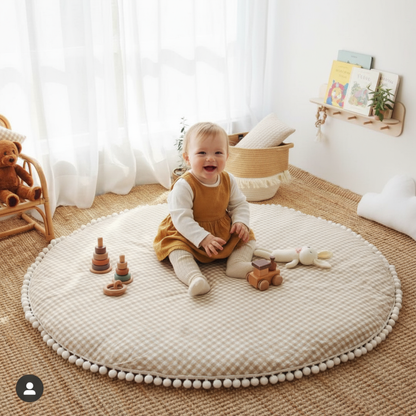 Child sitting on a round beige rug with toys in a room with white curtains and wooden furniture.