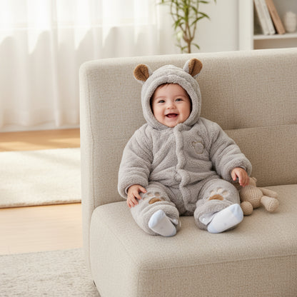 Baby in a bear-themed onesie sitting on a couch in a bright room.