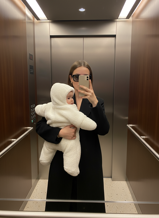 Person holding a baby wrapped in a white blanket inside an elevator.