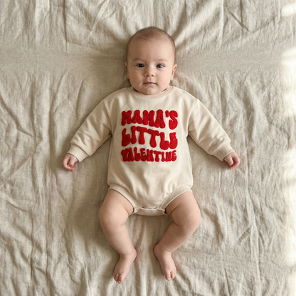 Baby wearing a onesie with 'Mama's Little Valentine' text on a beige blanket