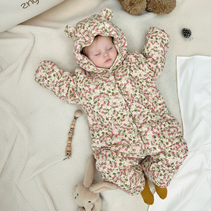 Baby in a floral onesie lying on a soft surface with toys around