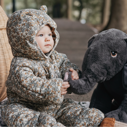 Child in floral snowsuit holding a plush elephant toy outdoors.