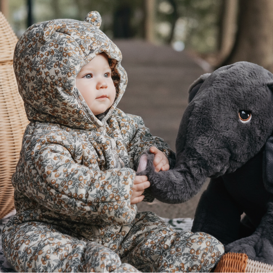 Child in floral snowsuit holding a plush elephant toy outdoors.