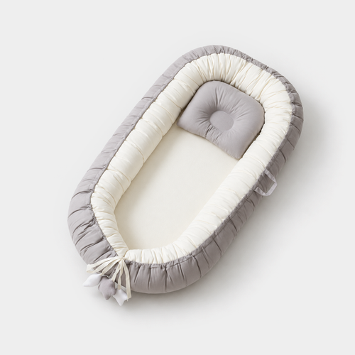 Gray and white baby nest with cushion on a beige background — studio view