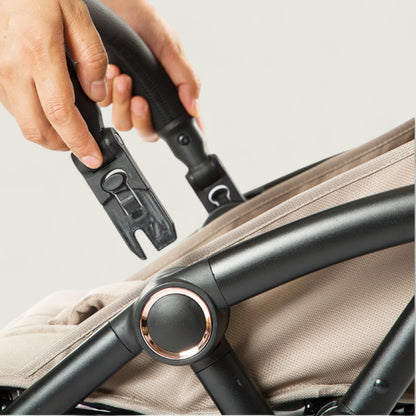 Close-up of a hand adjusting a stroller handle with a beige seat background