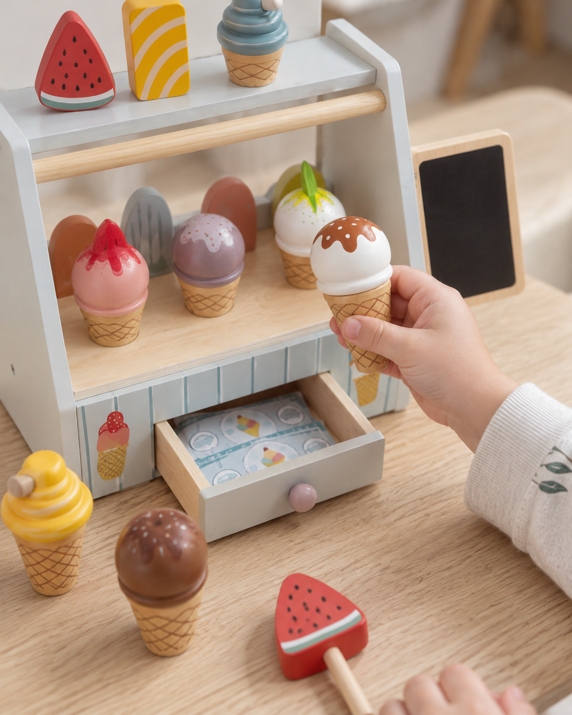 Child holding a wooden ice cream cone beside the stand and open play-money drawer