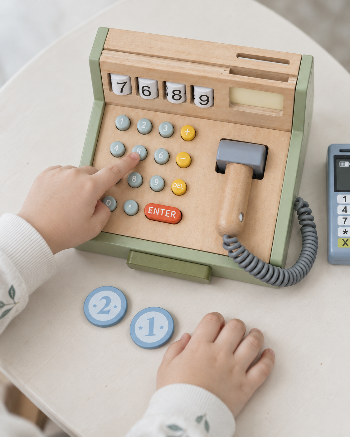 Child pressing a number key on the wooden cash register with pretend scanner and play coins