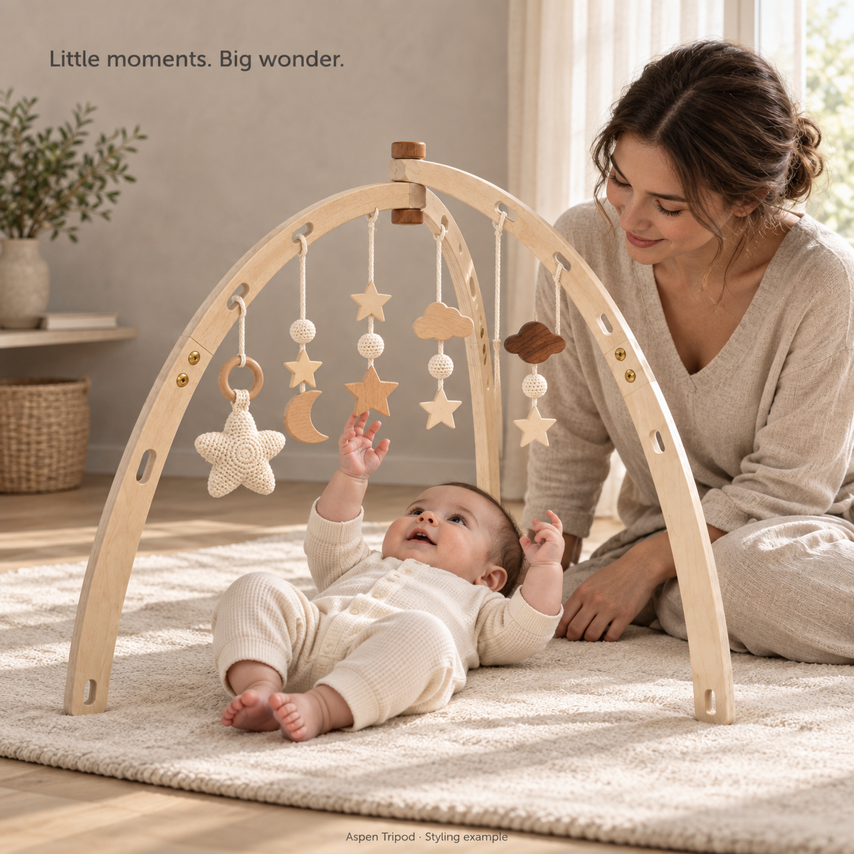 Aspen Tripod styling example with Star Dreams hanging toys, an awake baby on a floor mat and mother beside them. Accessories illustrate a styled setup.