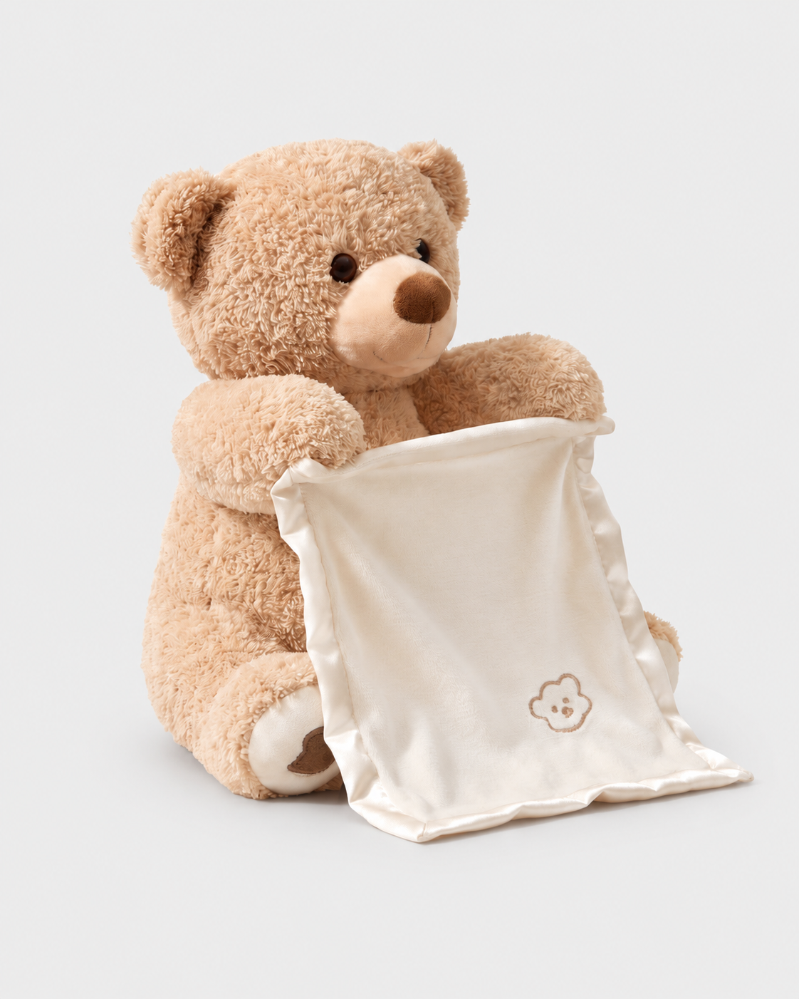 Peekaboo Bear holding its ivory cloth on a seamless light grey studio background