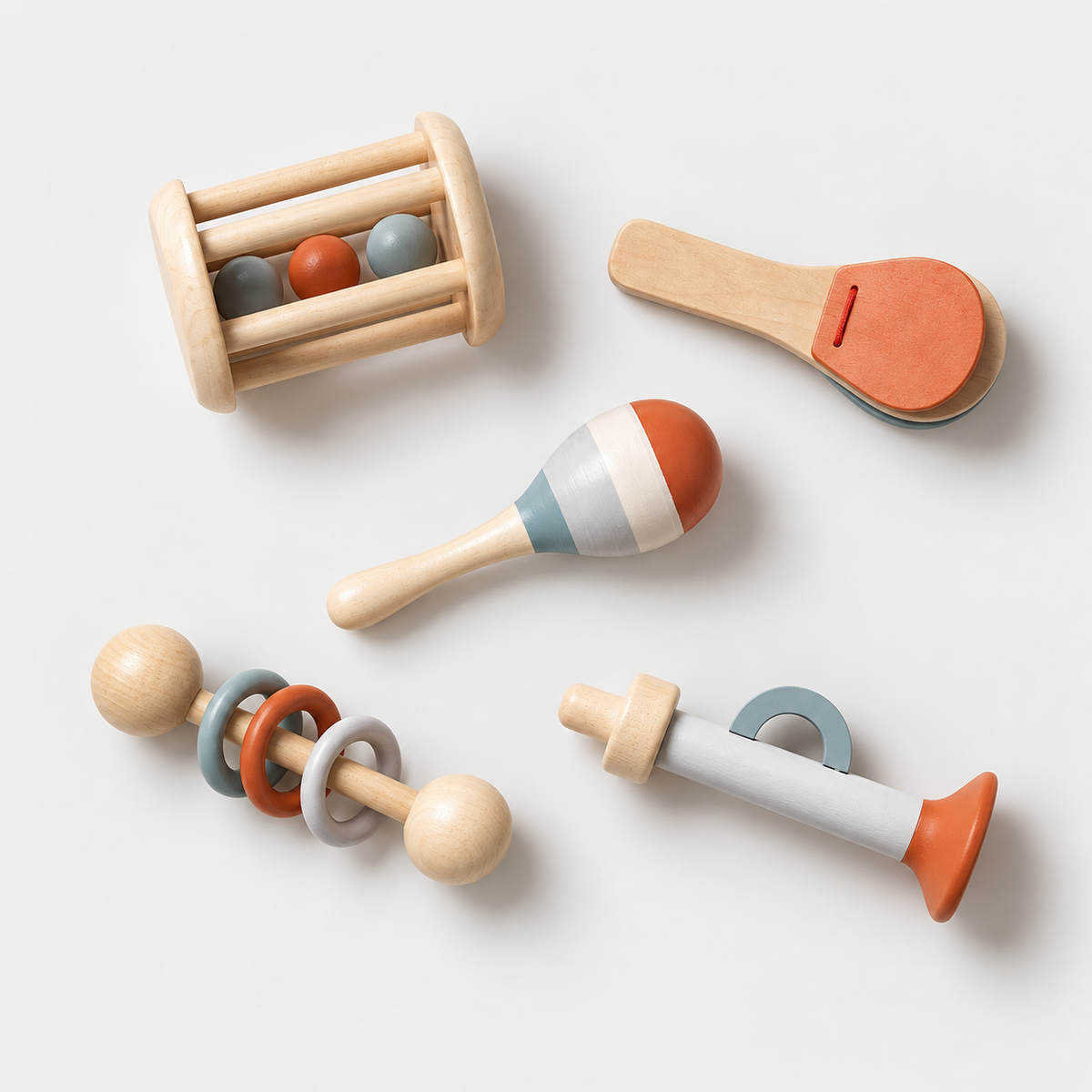 Five wooden toys arranged on a light grey studio background: roller, clapper, maraca, ring rattle and trumpet-shaped toy.
