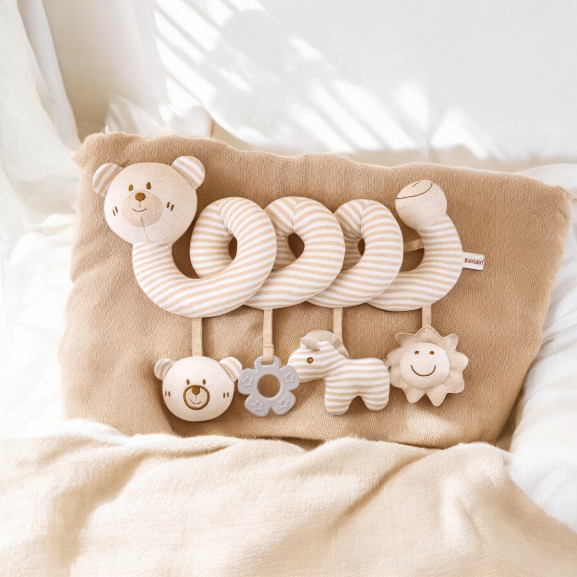 Baby comfort toy with soft textures and animal shapes on a beige pillow.