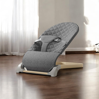 Gray baby bouncer chair on a wooden floor with white curtains in the background